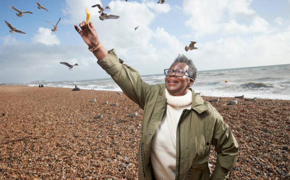 A woman on the beach holding a chip in the air to feed to the seagulls