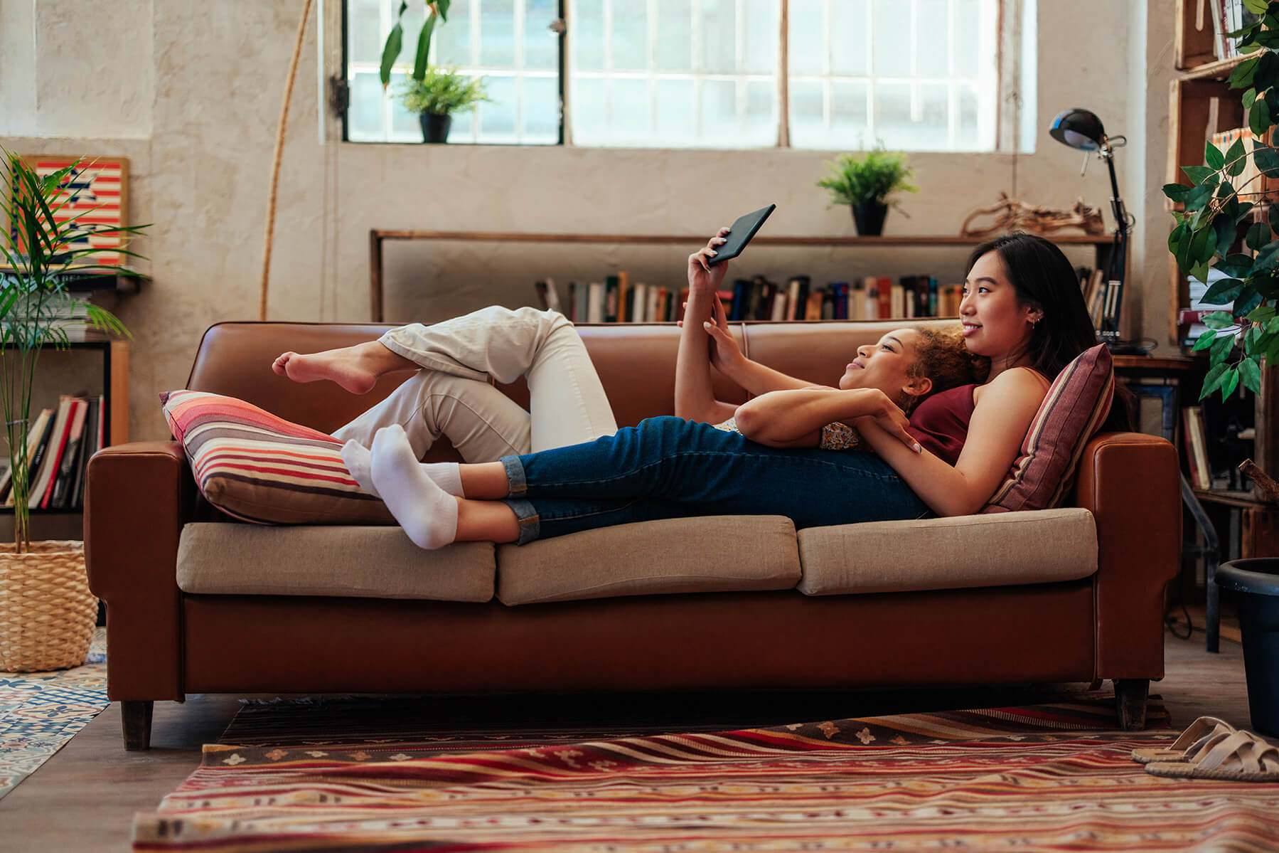 2 women lying on the sofa together both watching something on a tablet
